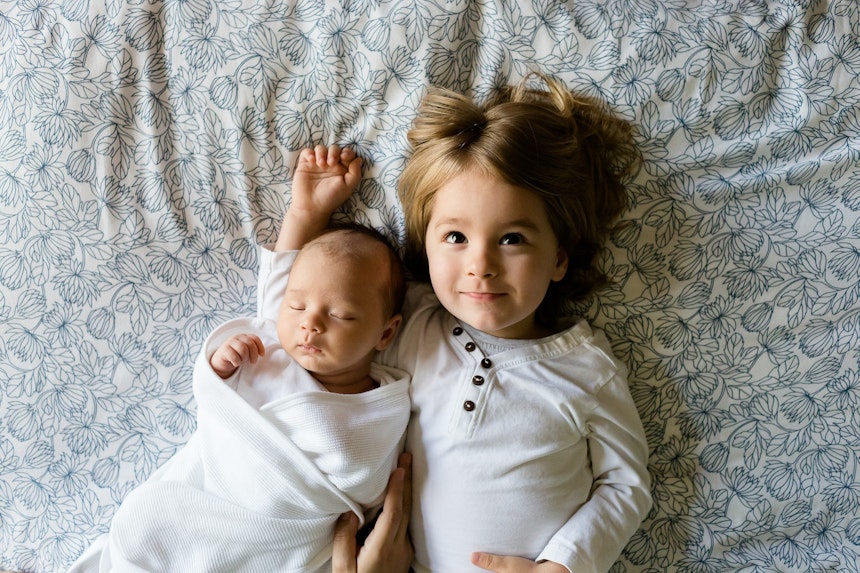 Two siblings lying on a bed.